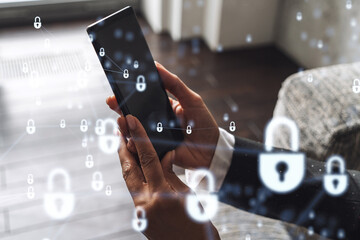 A woman programmer is browsing the Internet in smart phone to protect a cyber security from hacker attacks and save clients confidential data. Padlock Hologram icons over the typing hands. Formal wear