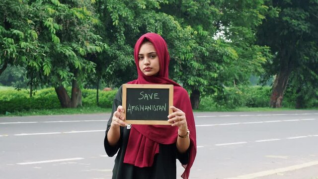 Kolkata, India : Attractive Afghan woman in hijab with a black sign board in her hands with written save Afghanistan, on a black background.
