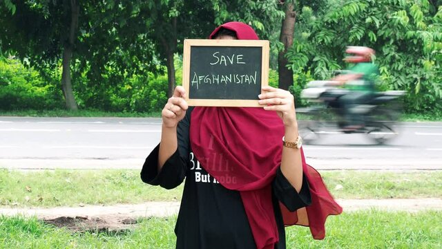 Kolkata, India : Attractive Afghan woman in hijab with a black sign board in her hands with written save Afghanistan, on a black background.