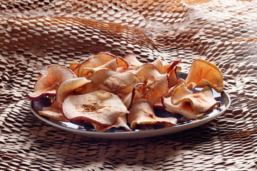 Dried apple chips in rustic plate. Soft focus.
