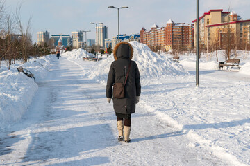 A woman walks along a snow-covered street in  city of Krasnoyarsk. View from back. Concept of winter season in Siberia.