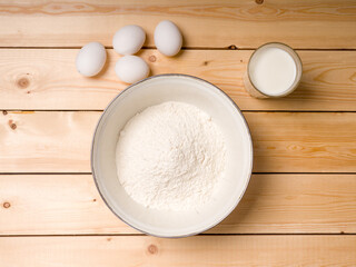 Flour, milk and eggs on a wooden background. Pancake baking ingredients. View from above