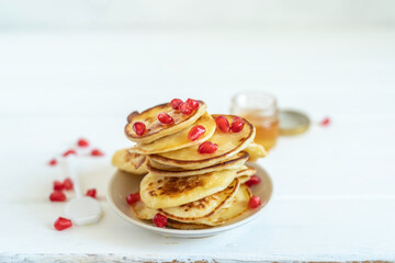 Miniature pancakes with fresh honey and pomegranate seeds for Jewish holiday Rosh Hashanah over white wooden background.