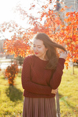 young woman with red lipstick in burgundy sweater in autumn park fixing hair 