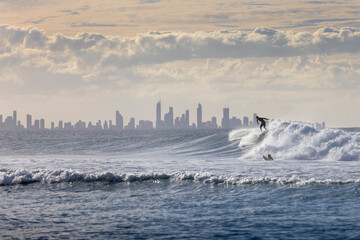 Unidentified surfers catching waves off Coolangatta Beach with the Gold Coast in the background at dusk