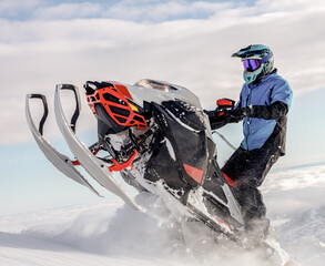 Fototapeta na wymiar a snowmobiler rides and jumps in the snowy mountains. prof pilot of a mountain snowmobile in bright gear without brands for travel advertising