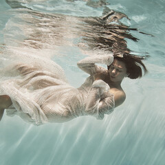 A girl in a blue dress swims underwater on a light background as if in weightlessness