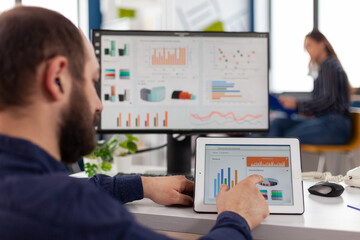 Fototapeta premium Businessman in wheelchair analyzing financial graph using tablet computer working at management statistics in startup company office. Handicapped disabled manager planning digital strategy