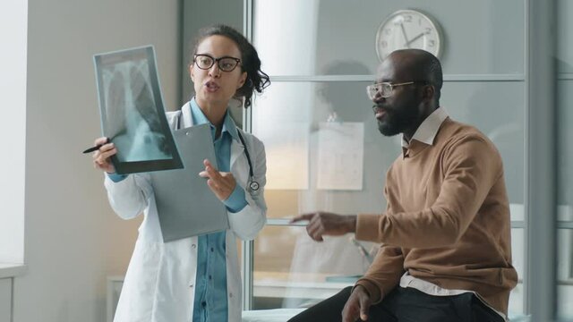 Female doctor explaining chest x-ray image to African American man during medical checkup in clinic
