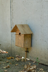 Unusually mounted birdhouse. A wooden birdhouse stands at the bottom of a concrete fence. Selective focus.