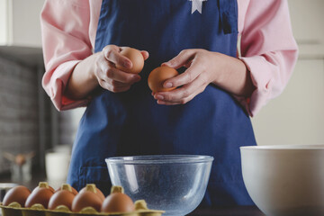 Woman baker in a blue apron breaks eggs for baking. Home cozy cooking aesthetics.