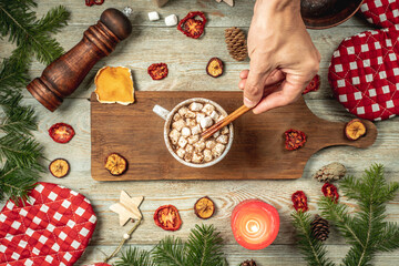 Hand is stirring hot chocolate decorated with marshmallows with a cinnamon stick. Concept of cozy...