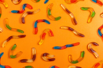Gummy worms for Halloween on orange background.