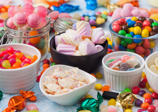 Jelly sugar gums candies on blue background with liquorice allsorts and strawberry marshmallow and large variety of sweets and candies.