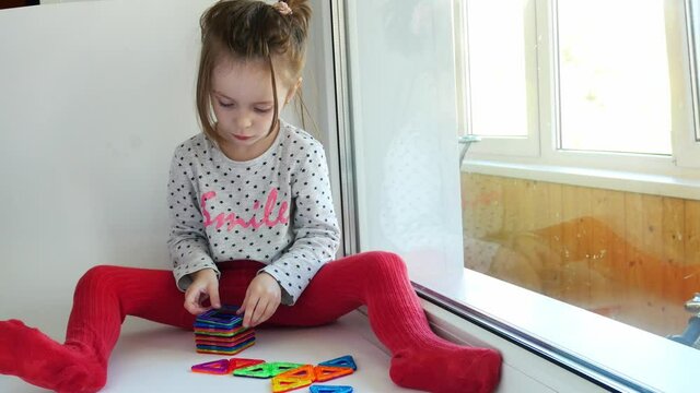 A little girl collects a figure from a magnetic constructor. Children's development, toys.