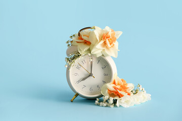 Alarm clock with beautiful flowers on blue background. Spring time concept