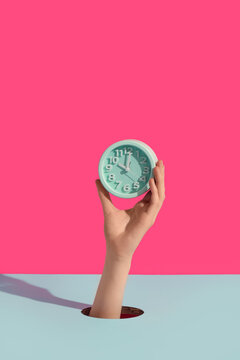 Female hands holding alarm clock through hole on color background