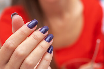 Girl's hand with dark purple nails on a red dress background
