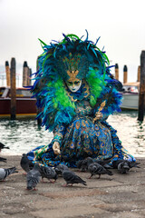 Woman in blue mask feed pigeons. Famous carnival in Venice, Italy