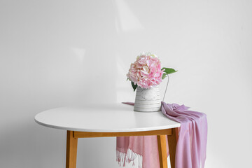 Vase with hydrangea flowers on table near light wall