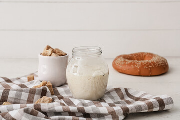Glass jar with fresh sourdough on white wooden background