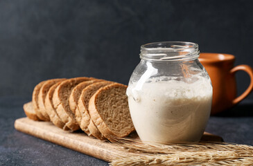 Jar with fresh sourdough and bread slices on black background