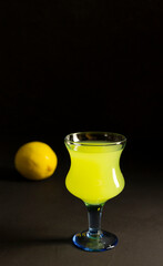 Limoncello Liqueur or poncha drink in a glass goblet with copy space with dark background and lemon