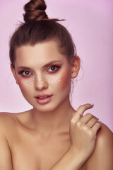 Beautiful portrait of young woman with fashion creative make up. Clean fresh skin and bright make up with rhinestones freckles on her face posing on a bright pink background