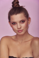 Beautiful portrait of young woman with fashion creative make up. Clean fresh skin and bright make up with rhinestones freckles on her face posing on a bright pink background