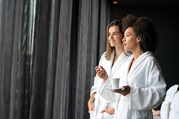 Lesbian couple relaxing and drinking tea in robes during wellness weekend