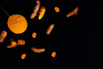 Turmeric (curcumin) powder in a wooden ladle and fresh rhizome on a black background, For spices and medicine.