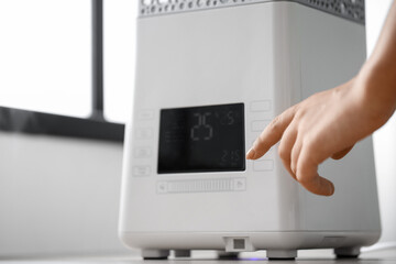 Woman switching on modern humidifier in room
