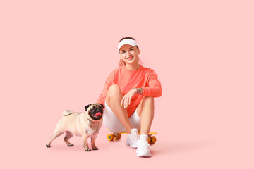 Young sporty woman with cute pug dog on pink background