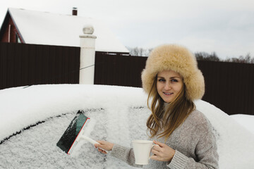 A girl in a winter hat with a mug of tea by a snow-covered car