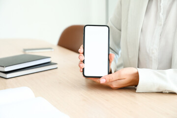 Businesswoman with mobile phone at table in office, closeup