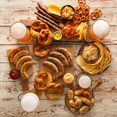 Glasses of cold beer, boards with Bavarian sausages and snacks on white wooden background. Oktoberfest celebration