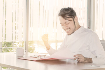 Asian businessman who sitting work in feeling happy at the office with daylight from window and blur garden background.