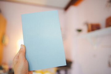 Hand holding a blue book with a blank cover for putting text in the room.