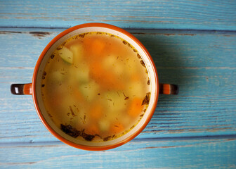 chicken broth with vegetables in a brown plate lies on a blue wooden table. top view. homemade food