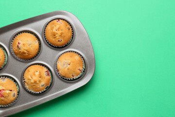 Baking tin with tasty cranberry muffins on color background, closeup