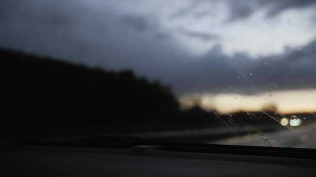 Driving on a highway in rain. First person view from inside the car. Windshield wipers move across the windscreen. Captured in slow motion at dusk. 