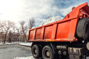 Tractor loader machine uploading dirty snow into dump truck. Cleaning city street, removing snow...