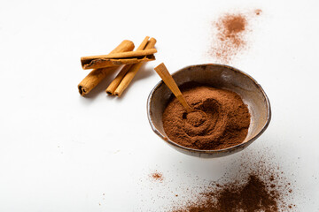 Cinnamon sticks and powder in bowl white surface copy space