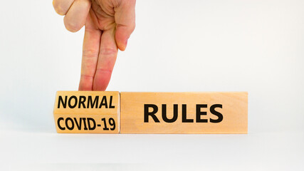 Symbol of covid-19 or normal rules. Doctor turns a wooden cube and changes words 'covid-19 rules'...