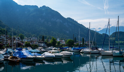Fototapeta na wymiar Early morning in harbor. Сoastal town Gersau of Lake Lucerne and Swiss Alps. A lot of white boats and luxury yachts moored in marina on a turquoise water, during a summer season. Travel and vacation.