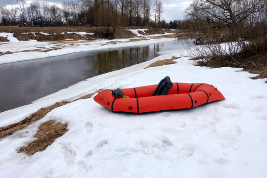 Red packraft on a snow-covered river bank in early spring. Packrafting. Active lifestile concept. 