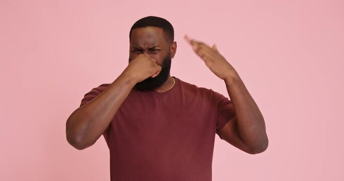 Young African american man on pink background holding breath with fingers on nose