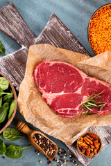 Fresh raw rib-eye steak on wooden cutting board.