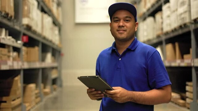 Supply chain. Young worker in blue uniform checklist manage parcel box product in warehouse. Asian man employee thumbs up using tablet working at store industry. Distribution warehouse import export