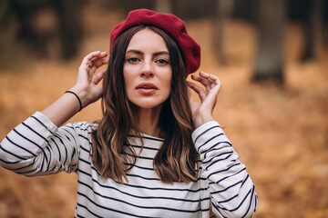 Portrait of brunette woman in autumn in the park. French style. Woman in beret and striped blouse